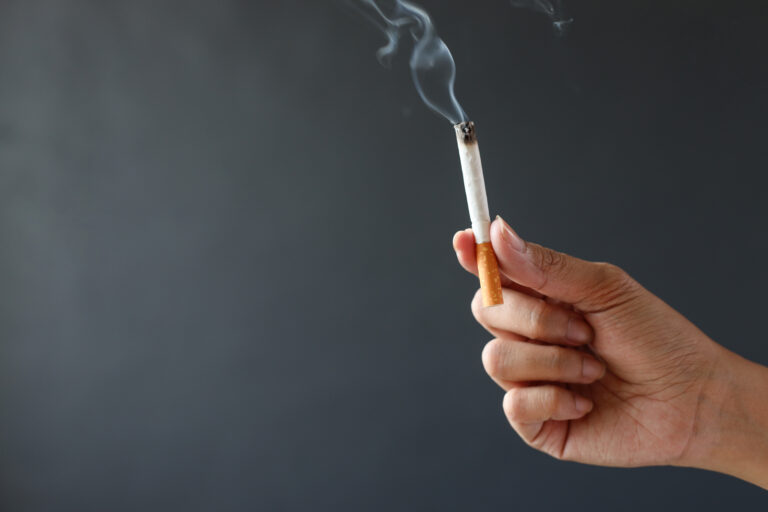 Mano con cigarrillo encendido — el tabaco daña los dientes y las encías